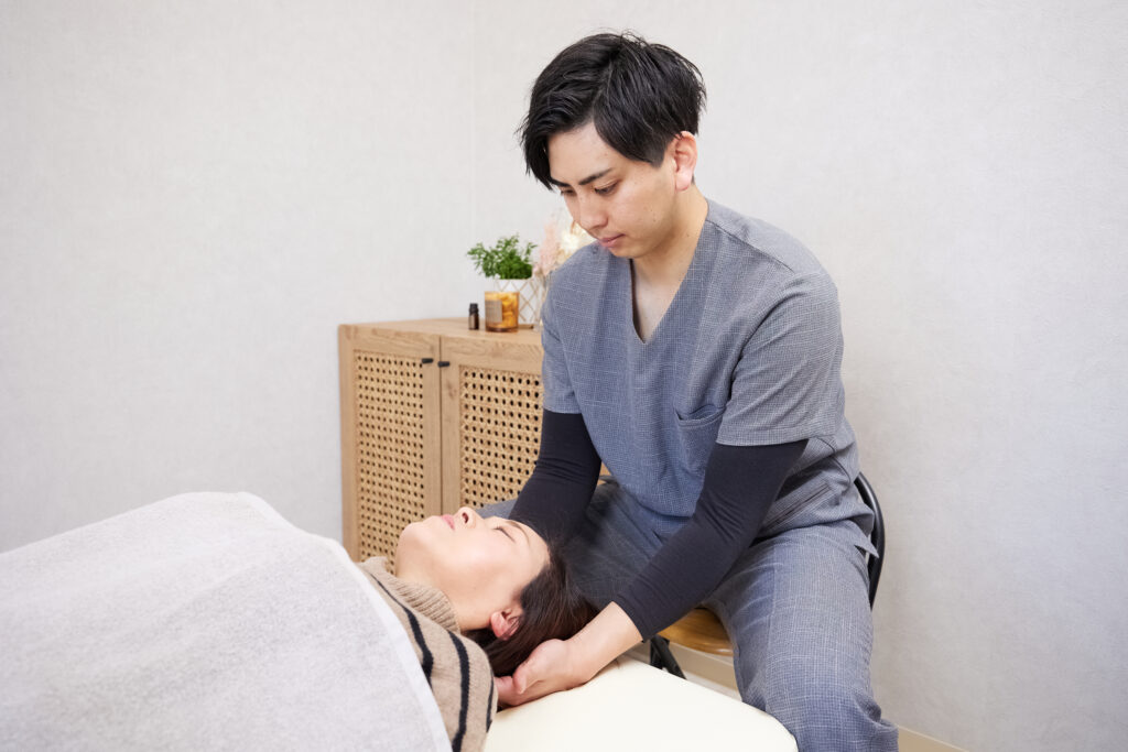 仰向けに寝た女性の首を施術する施術者