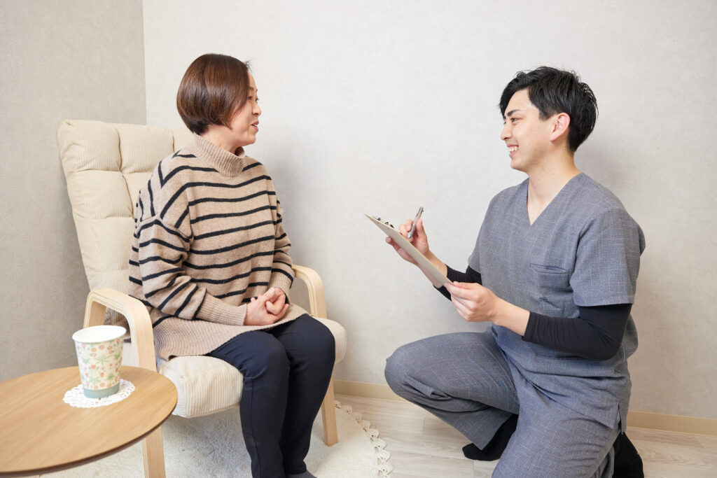 椅子に座った女性に今後の施術方針を説明する施術者